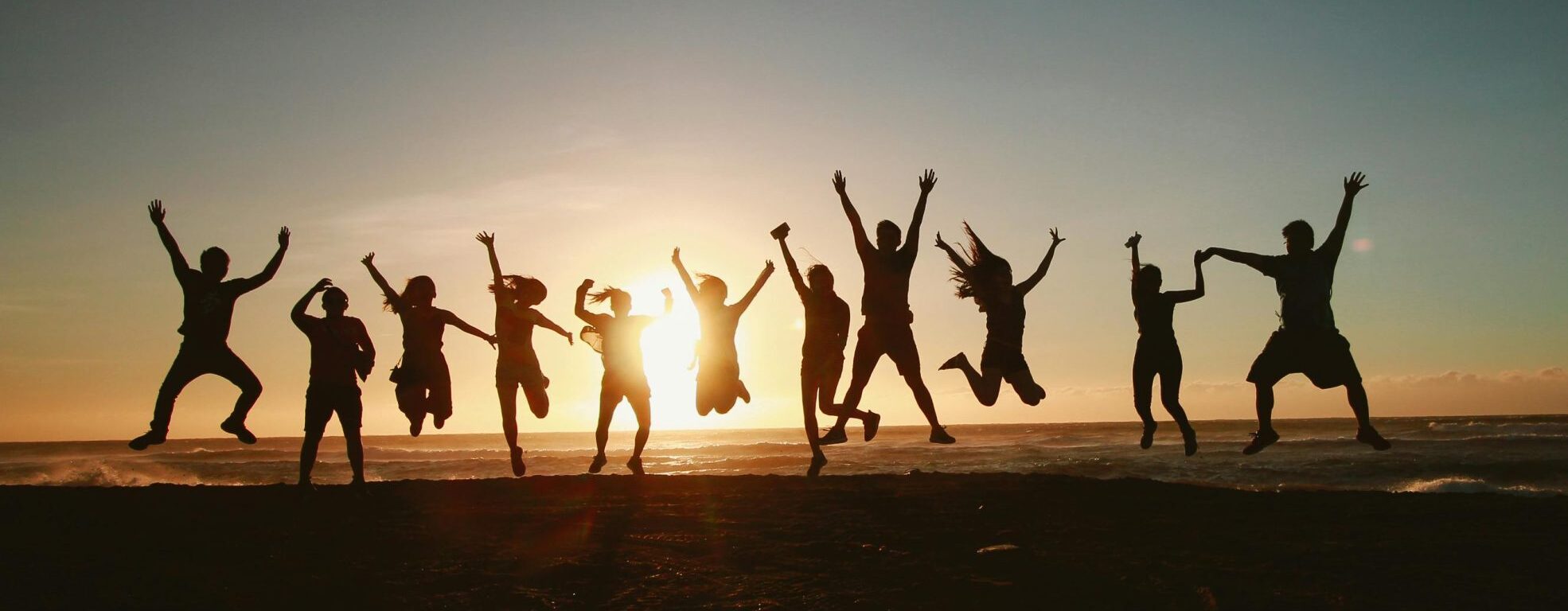 Silhouette of a group of friends jumping on a beach at sunset, expressing joy and freedom.
